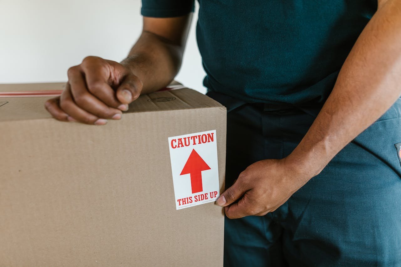 A person handling a moving box with a caution this side up label indoors.